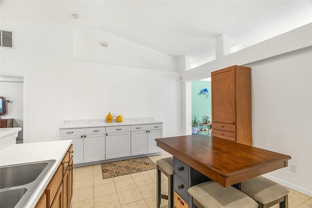 kitchen featuring a sink, white cabinetry, light countertops, light tile patterned floors, and vaulted ceiling