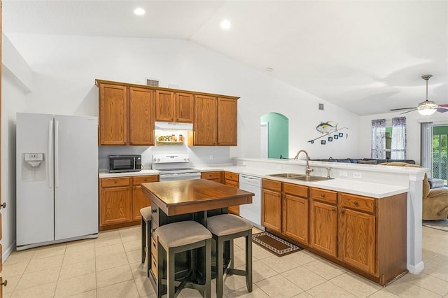 kitchen with white appliances, brown cabinetry, a peninsula, a sink, and under cabinet range hood