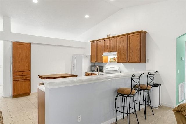 kitchen featuring a kitchen bar, under cabinet range hood, white fridge with ice dispenser, a peninsula, and range