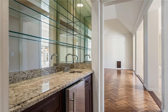 bar with lofted ceiling, sink, light stone countertops, parquet flooring, and dark brown cabinetry