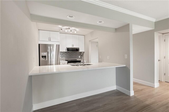 kitchen with sink, appliances with stainless steel finishes, kitchen peninsula, white cabinets, and backsplash