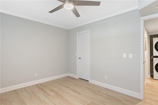 spare room with stacked washer / drying machine, crown molding, ceiling fan, and light wood-type flooring