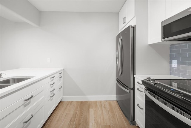 kitchen featuring appliances with stainless steel finishes, tasteful backsplash, sink, white cabinets, and light hardwood / wood-style flooring