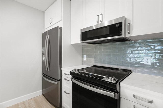 kitchen with appliances with stainless steel finishes, light stone countertops, backsplash, white cabinets, and light wood-type flooring