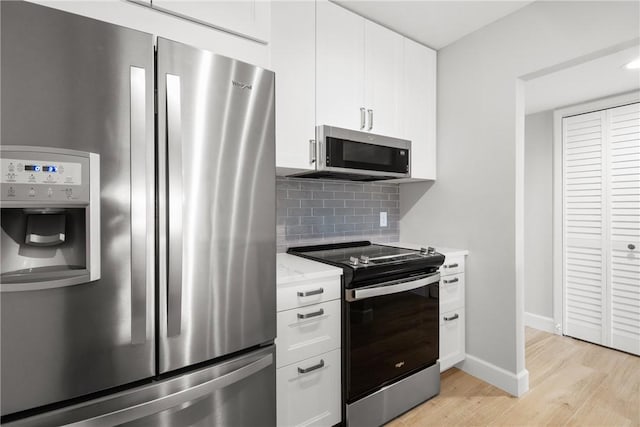 kitchen featuring appliances with stainless steel finishes, white cabinetry, backsplash, light stone counters, and light wood-type flooring