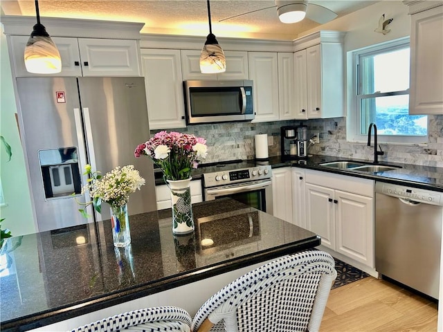 kitchen with white cabinetry, sink, stainless steel appliances, and decorative light fixtures