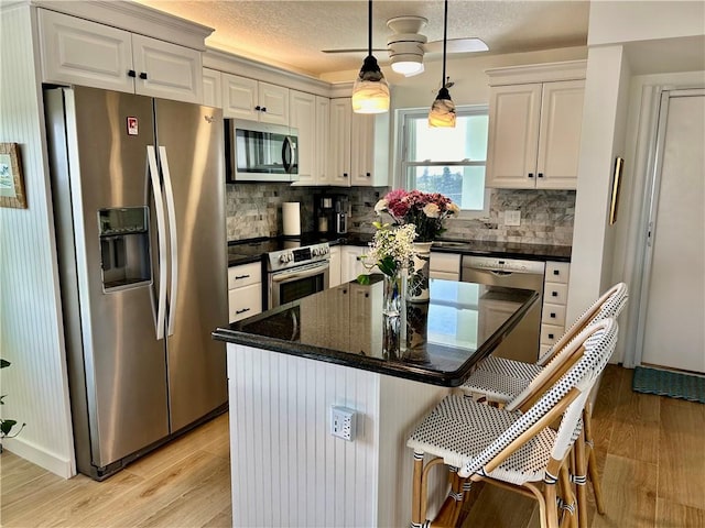 kitchen with appliances with stainless steel finishes, decorative light fixtures, light hardwood / wood-style flooring, and white cabinets