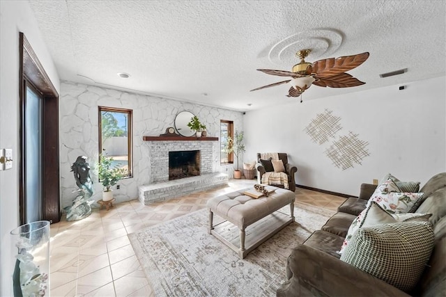 living area with a textured ceiling, a fireplace with raised hearth, and ceiling fan