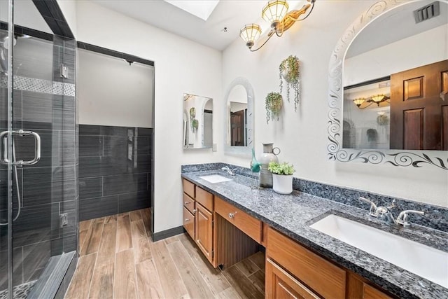 full bathroom with wood finished floors, a shower stall, double vanity, and a skylight