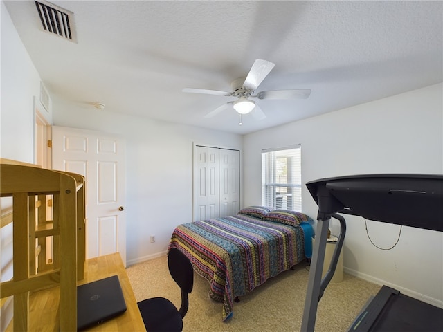 bedroom featuring ceiling fan, light colored carpet, a textured ceiling, and a closet