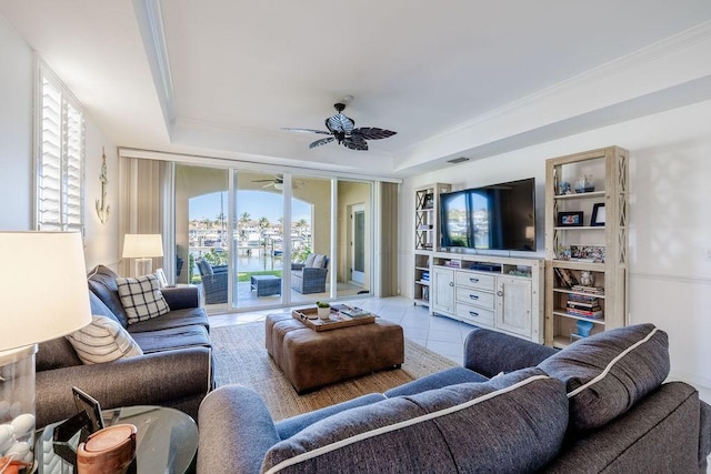 living area featuring a tray ceiling, ornamental molding, light tile patterned floors, and ceiling fan