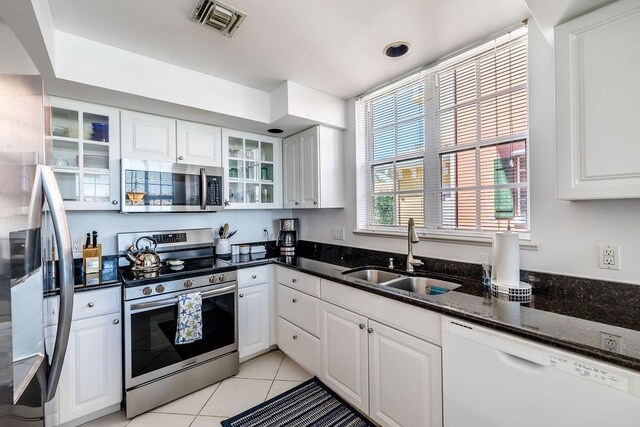 kitchen with dark stone counters, light tile patterned flooring, a sink, stainless steel appliances, and white cabinetry