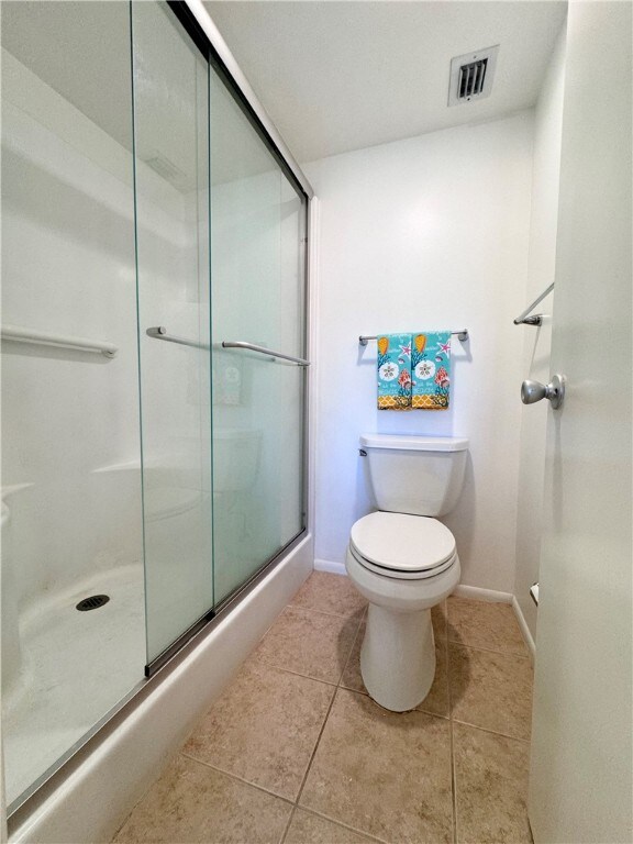 full bath with toilet, visible vents, baseboards, tile patterned floors, and an enclosed shower