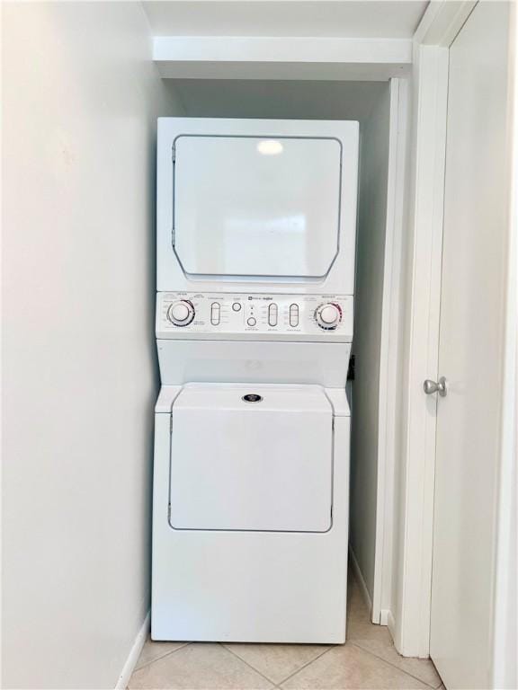 laundry area featuring stacked washer and dryer, baseboards, light tile patterned floors, and laundry area