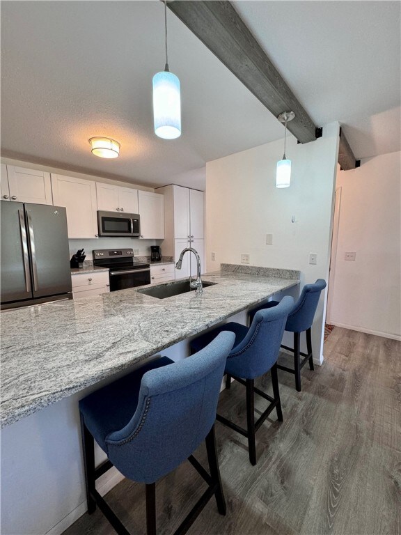 kitchen with stainless steel appliances, a peninsula, a sink, white cabinets, and hanging light fixtures