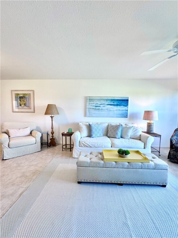 living room with tile patterned flooring, ceiling fan, and a textured ceiling