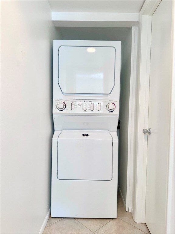 washroom with light tile patterned floors, baseboards, laundry area, and stacked washer and clothes dryer