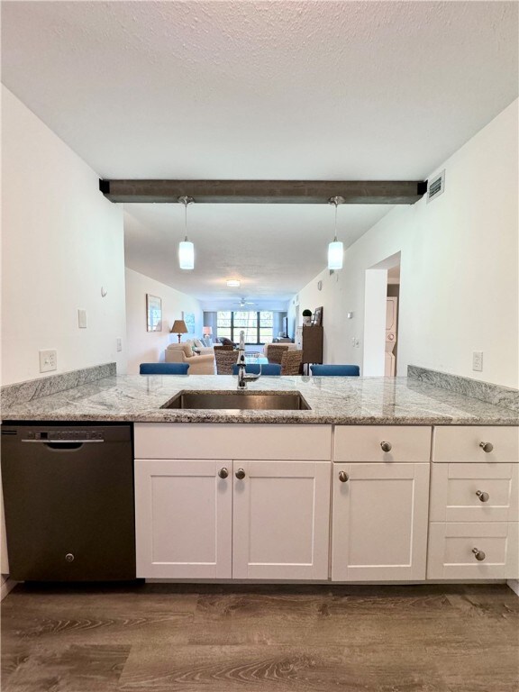 kitchen with black dishwasher, white cabinets, open floor plan, hanging light fixtures, and a sink