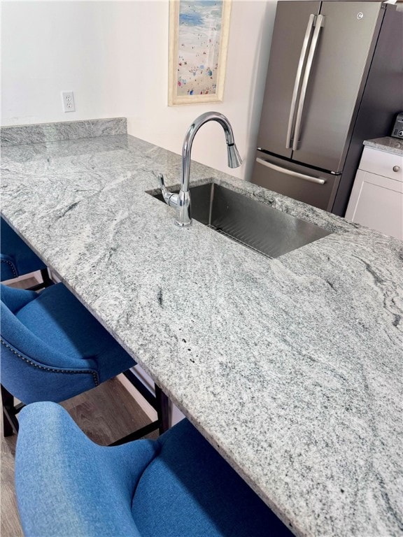 kitchen with white cabinetry, sink, stainless steel fridge, and wood-type flooring