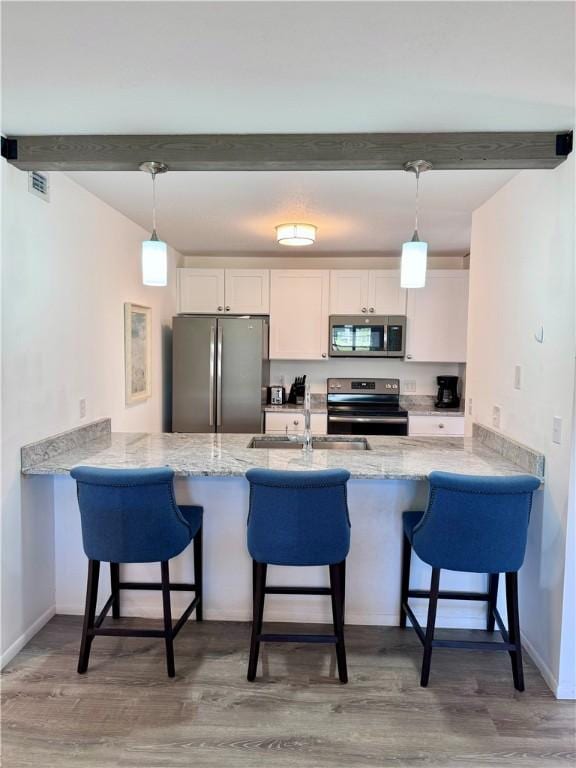 kitchen with stainless steel appliances, hanging light fixtures, white cabinetry, a sink, and a peninsula