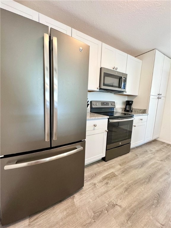 kitchen with white cabinets, appliances with stainless steel finishes, a textured ceiling, and light hardwood / wood-style floors