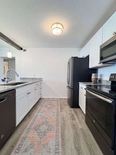 kitchen with white cabinets, appliances with stainless steel finishes, a textured ceiling, and light hardwood / wood-style floors