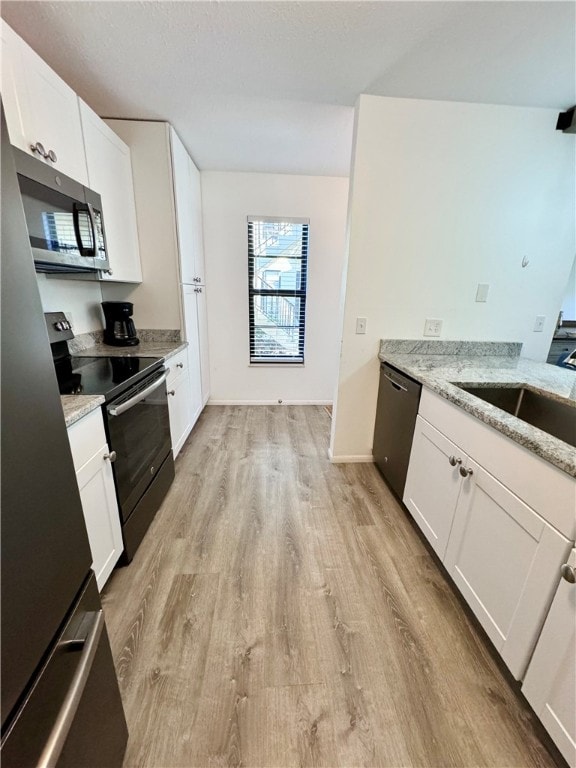 kitchen featuring light hardwood / wood-style flooring, appliances with stainless steel finishes, light stone counters, and white cabinets