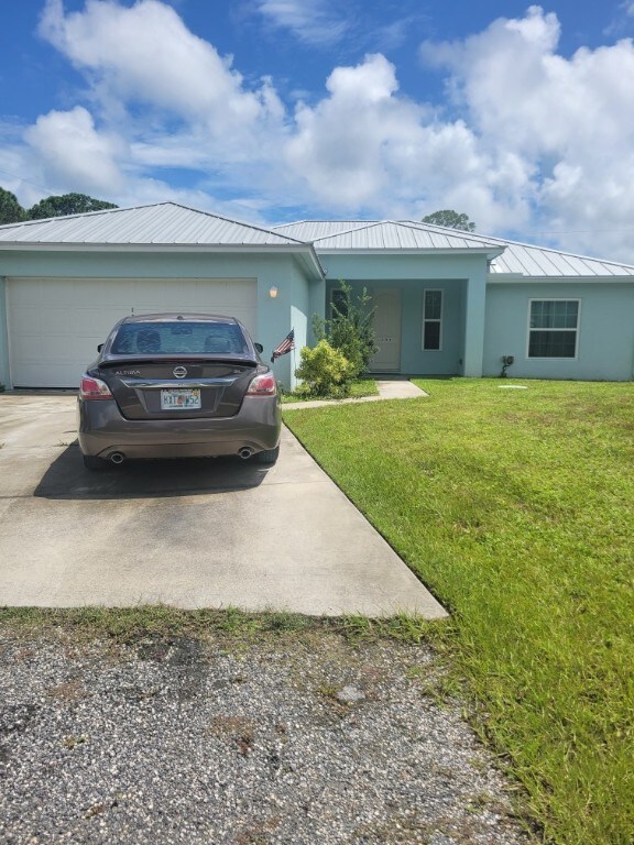 1204 38th Ave SW, Vero Beach, FL 32968 - ranch-style home featuring driveway, stucco siding, a front yard, a garage, and a standing seam roof