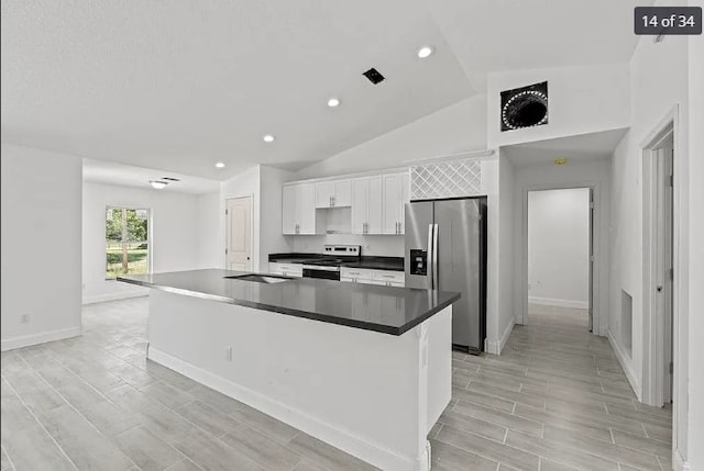 kitchen with light wood-type flooring, stainless steel appliances, a center island with sink, white cabinets, and lofted ceiling