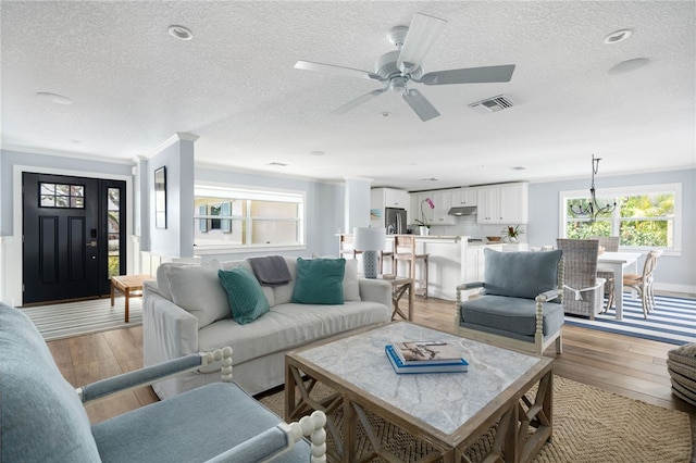 living room featuring crown molding, light wood-style flooring, visible vents, and a textured ceiling