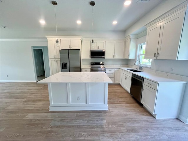 kitchen with a sink, baseboards, hanging light fixtures, appliances with stainless steel finishes, and a center island