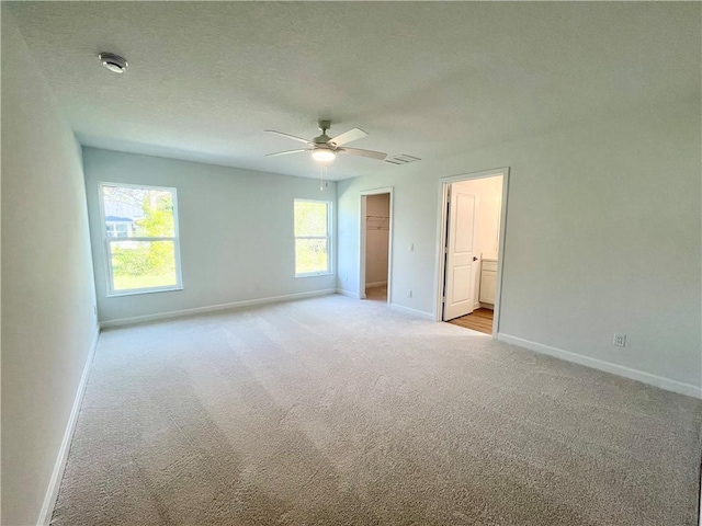 unfurnished bedroom featuring a textured ceiling, light colored carpet, visible vents, baseboards, and a walk in closet