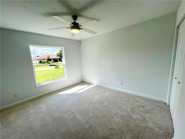 carpeted empty room with a ceiling fan and baseboards