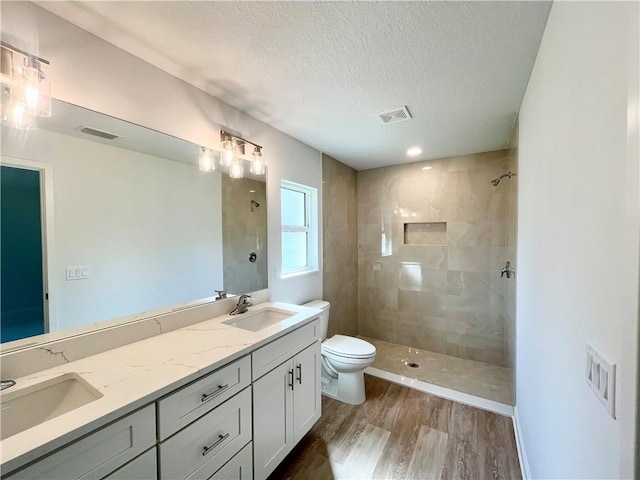 bathroom featuring visible vents, toilet, a sink, a tile shower, and wood finished floors