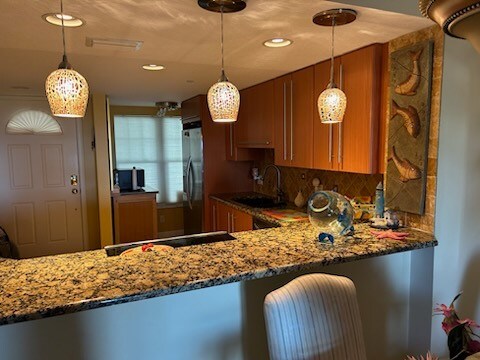 kitchen featuring white refrigerator, sink, tasteful backsplash, stone countertops, and pendant lighting