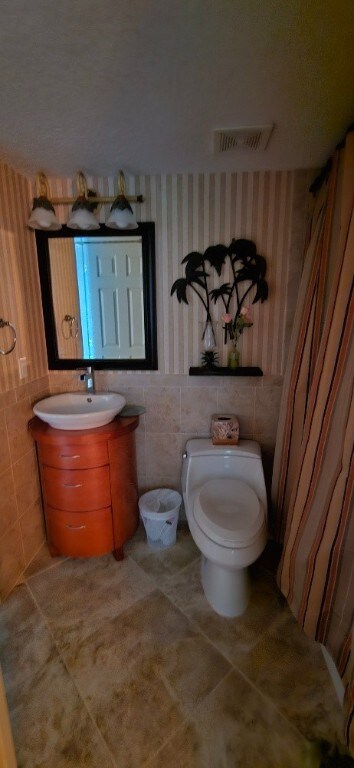 bathroom with vanity, tile patterned flooring, toilet, and tile walls