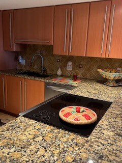 kitchen featuring decorative backsplash, black range oven, sink, and light stone counters