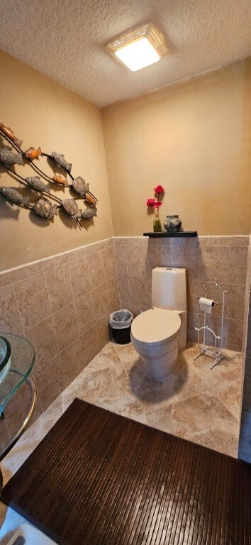 bathroom with toilet, tile walls, and a textured ceiling