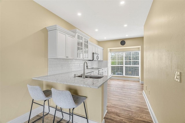 kitchen with a kitchen bar, light stone counters, kitchen peninsula, stainless steel appliances, and white cabinets