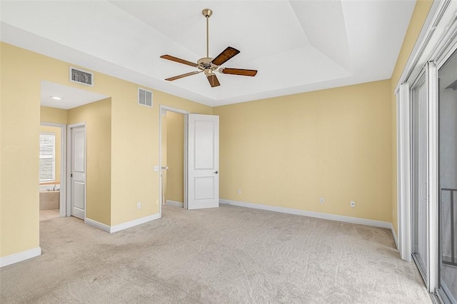 unfurnished bedroom featuring ceiling fan, a raised ceiling, and light carpet