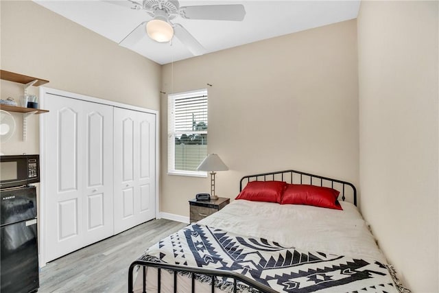 bedroom with light wood-type flooring, a closet, black fridge, and ceiling fan