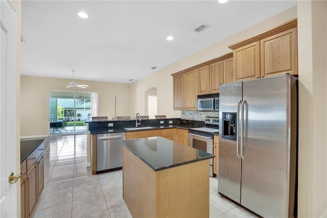 kitchen with light tile patterned floors, kitchen peninsula, appliances with stainless steel finishes, a center island, and sink