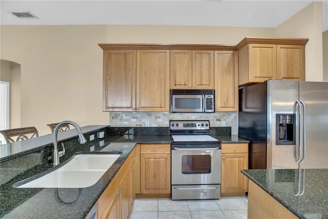 kitchen with light tile patterned floors, stainless steel appliances, decorative backsplash, dark stone countertops, and sink