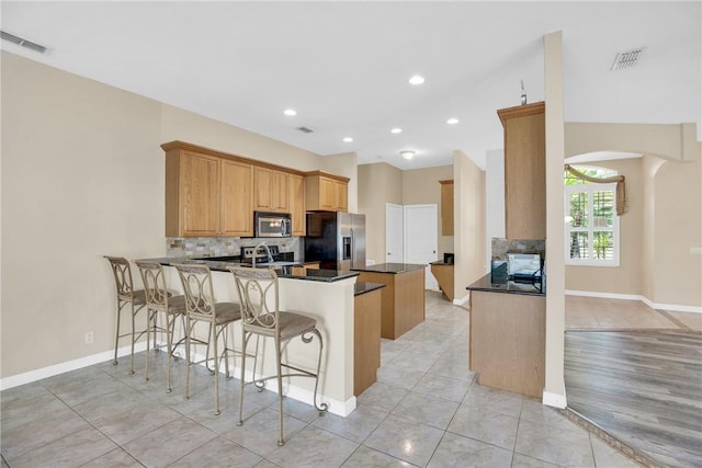 kitchen with light tile patterned floors, kitchen peninsula, stainless steel appliances, decorative backsplash, and a kitchen breakfast bar