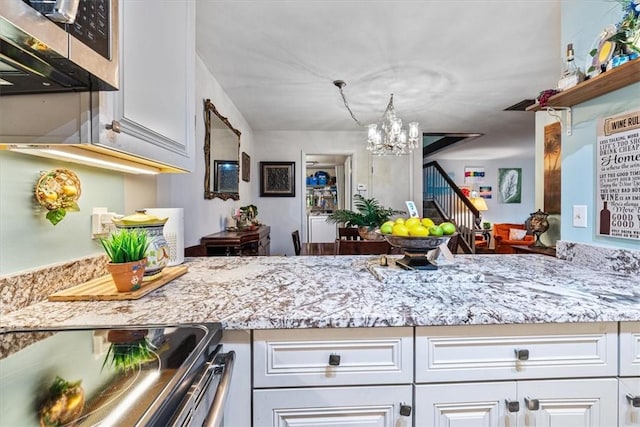 1170 6th Ave Unit 9D, Vero Beach, FL 32960 - kitchen with stainless steel microwave, range with electric stovetop, a chandelier, white cabinetry, and light stone countertops