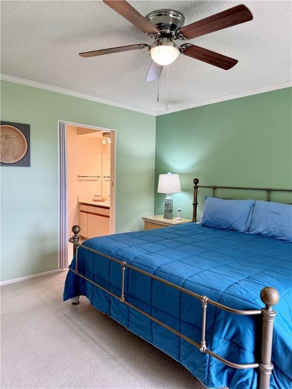 bedroom with carpet flooring, ensuite bath, ceiling fan, a textured ceiling, and ornamental molding