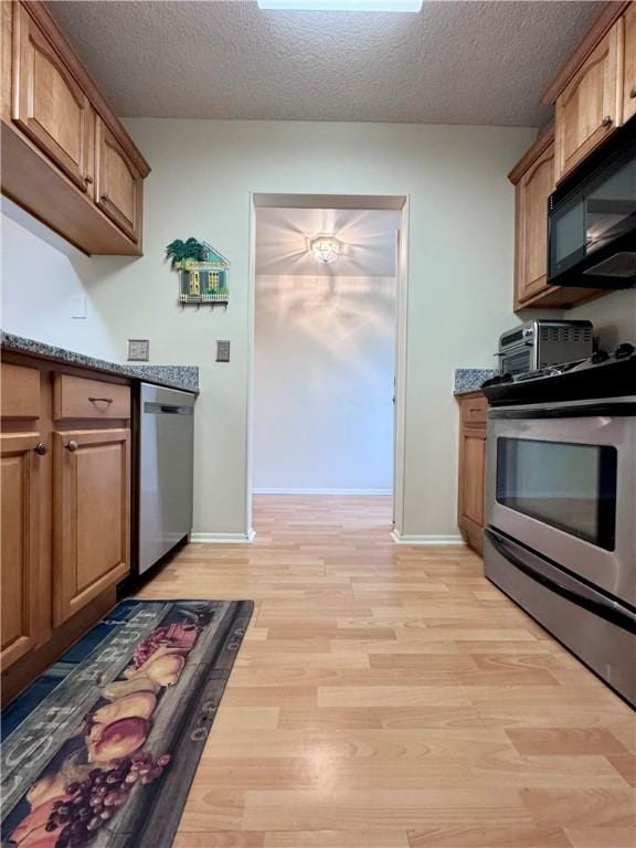 kitchen with light hardwood / wood-style floors, dark stone countertops, a textured ceiling, and appliances with stainless steel finishes