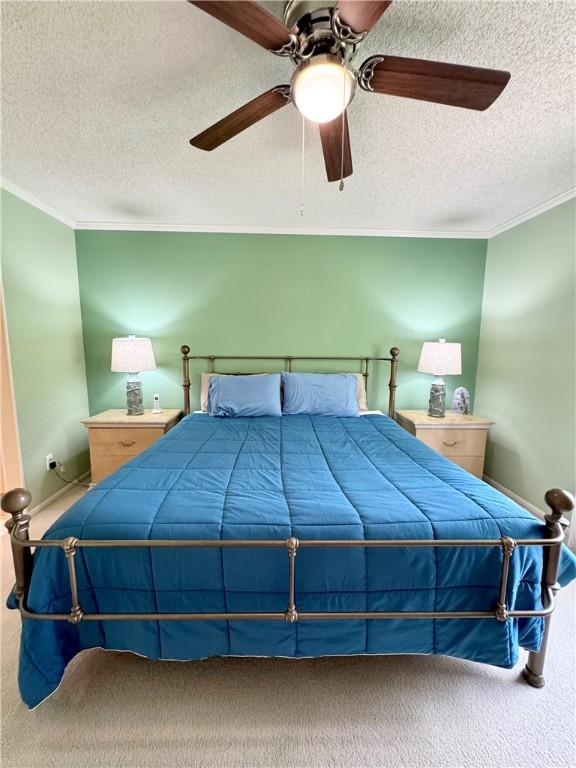 bedroom with ceiling fan, carpet, a textured ceiling, and ornamental molding