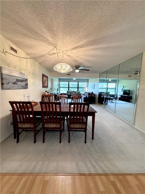 carpeted dining space featuring a textured ceiling and ceiling fan with notable chandelier