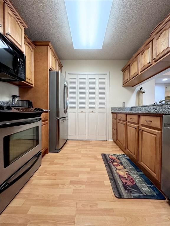 kitchen featuring stone counters, light hardwood / wood-style floors, a textured ceiling, and appliances with stainless steel finishes